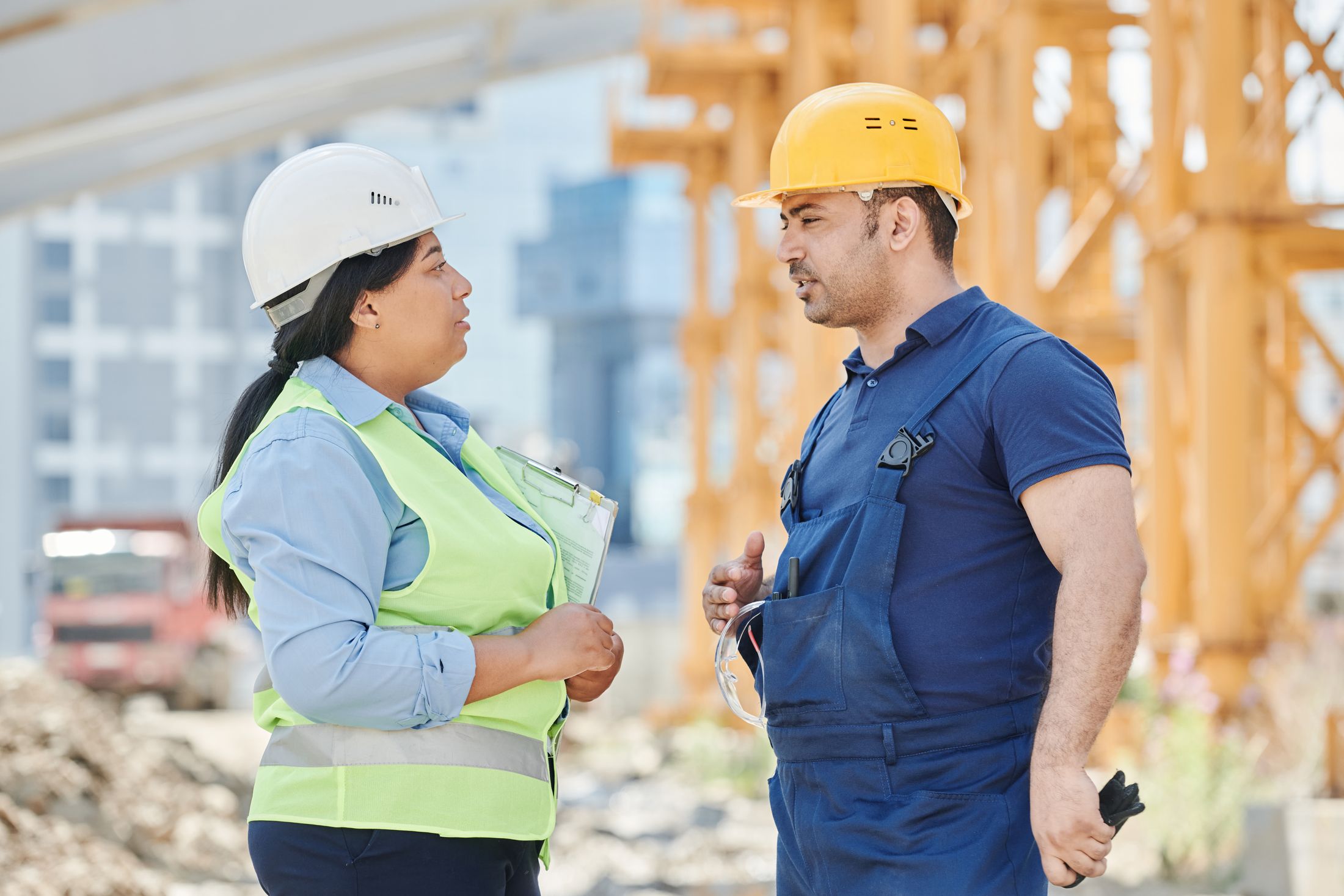 Profissionais com capacetes conversam em um canteiro de obras.