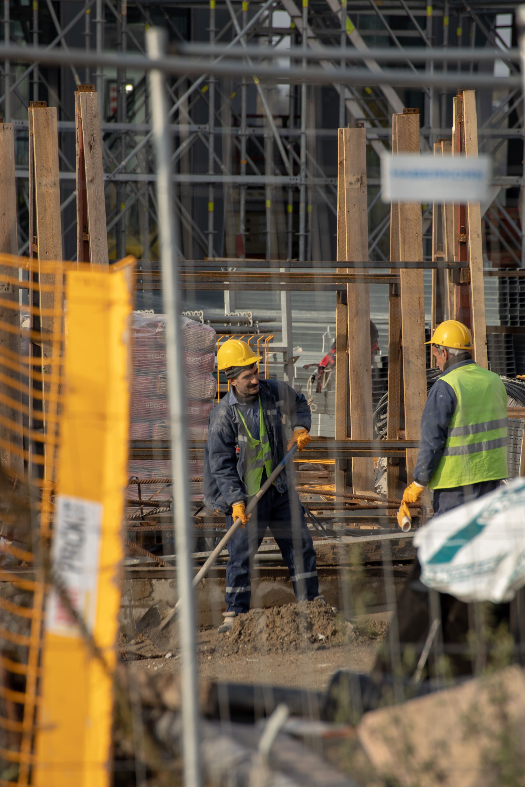 Dois trabalhadores com capacetes e luvas em uma estrutura de concreto.